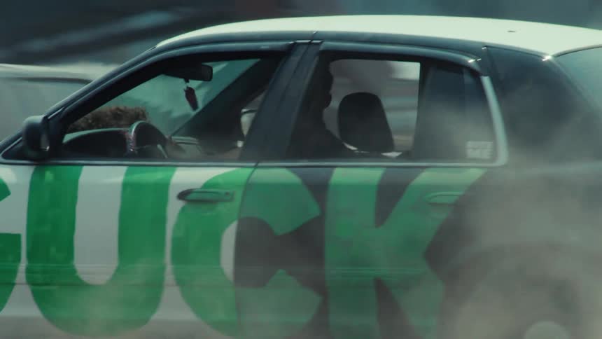 Slow motion shot of a demolition derby car driving past the camera on a dusty, rugged terrain