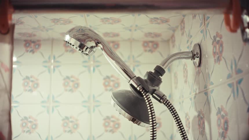 A close-up shot of a leaky shower head dripping water in a bathroom with patterned tiles
