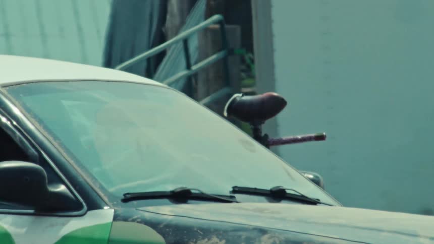 A silhouetted driver waits in a customized combat car with a paintball gun mounted on the hood in a slow-motion pan