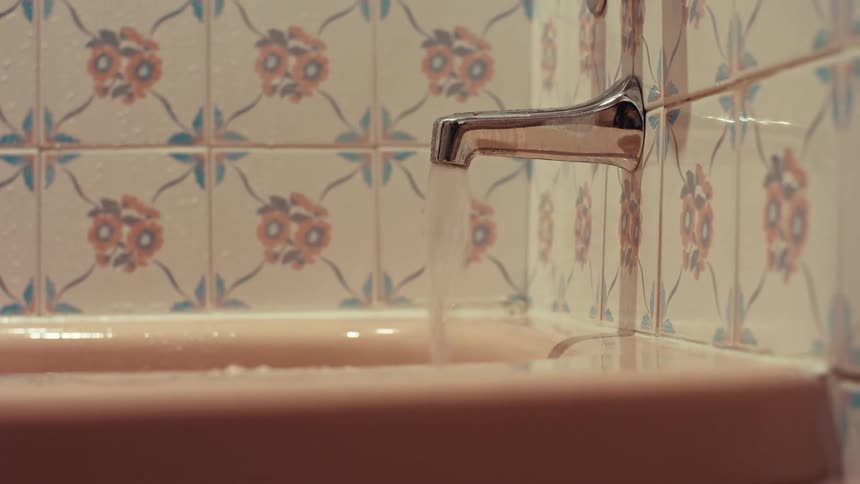 A hand reaches in to grab a bar of soap from the edge of a retro bathtub as it fills with water