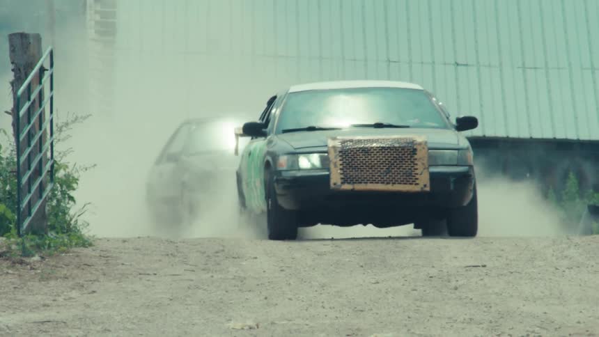 Two souped-up race cars kick up clouds of dust as they speed down a gritty farm road in slow motion