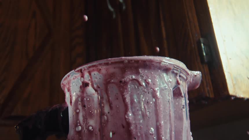 A close up, low angle view of a messy berry smoothie exploding from the top of a blender in super slow motion