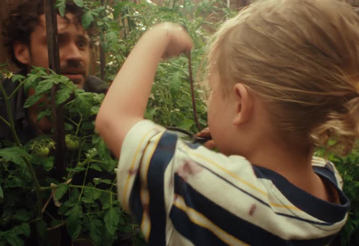 A young boy playfully teases his father with a worm while they explore the garden together