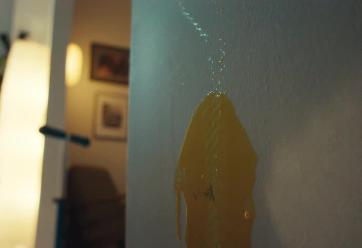 Close up in slow motion of an egg splattering against an interior wall and dripping down
