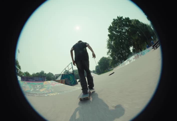 A stylish skateboarder executes a smooth trick over a ramp in a skatepark, filmed in slow motion with a classic fisheye lens