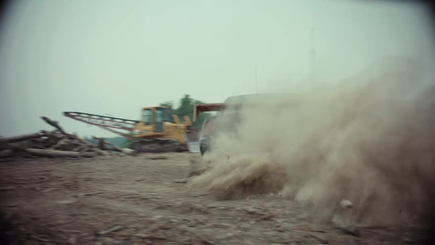 A modified sedan with green graffiti drifts in slow motion on a dirt road, kicking up a massive cloud of dust that engulfs the camera