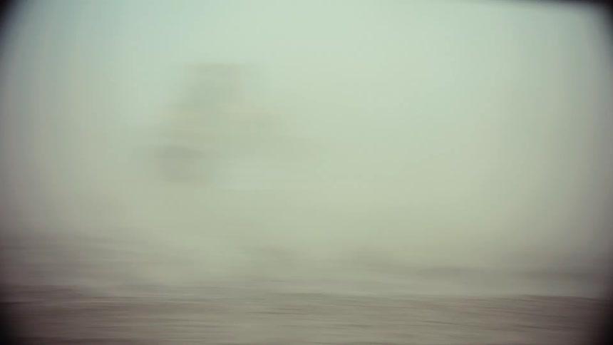 Slow motion of two souped-up cars driving through a dusty wasteland as men shoot paintball guns from the windows