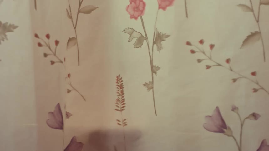 A soap bottle sits on the edge of a vintage pink bathtub as the floral shower curtain is pulled shut