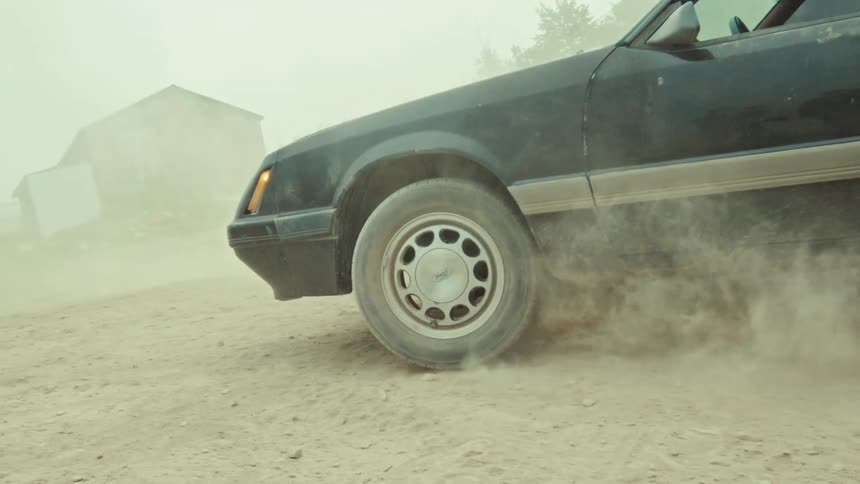 Slow motion shot of a black vintage car's tire kicking up a large cloud of dust as it spins out on a dirt road