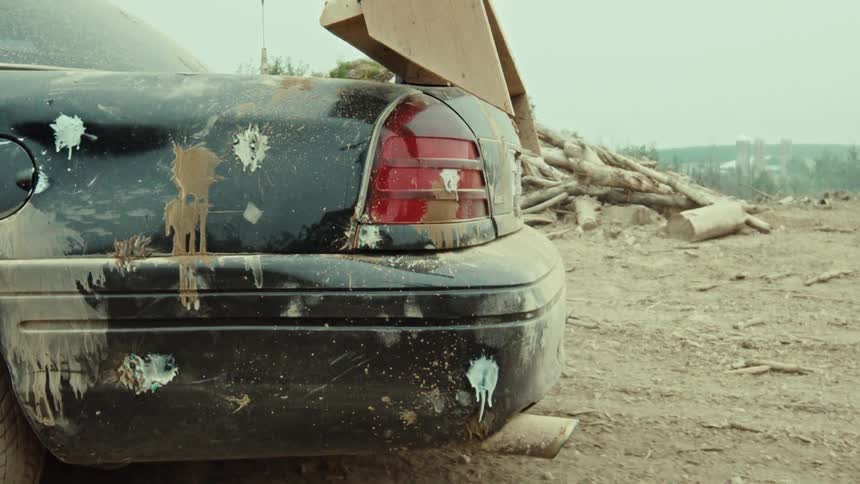 Close up on the muddy back bumper of a black car with a homemade wooden spoiler and paintball splatters