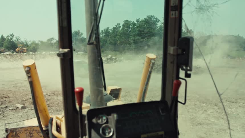 View from a bulldozer cab with a cracked windshield as a demolition derby car crashes, sending dust flying
