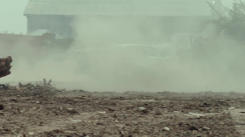A modified derby car speeds through a dusty junkyard, kicking up debris in a dramatic slow-motion shot
