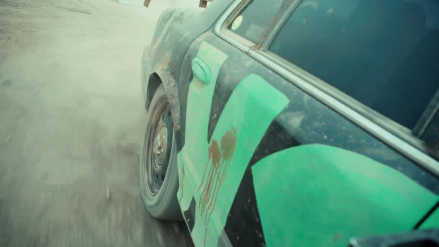 Close up shot of a beat-up car tire spinning in dust and mud during a demolition derby in slow motion