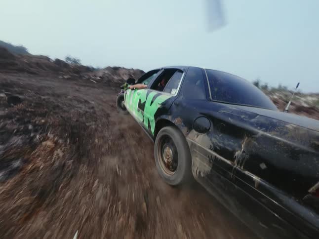 A modified car with green graffiti speeds down a dusty road while a person aims a paintball gun out the window in a seamless loop