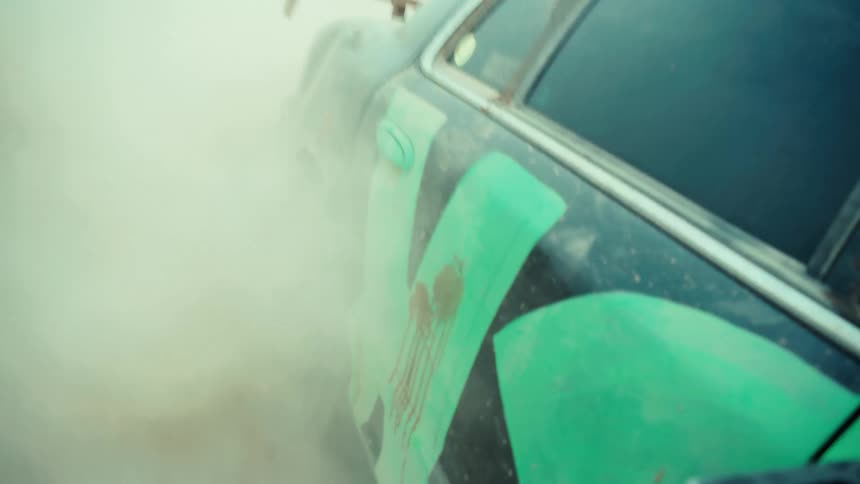 Slow motion close-up of a rugged car's rear wheel spinning out and creating a massive cloud of dust on a dirt track