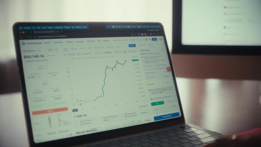 A slow zoom shot focuses on a laptop screen displaying a dynamic cryptocurrency trading chart as a person analyzes the financial data