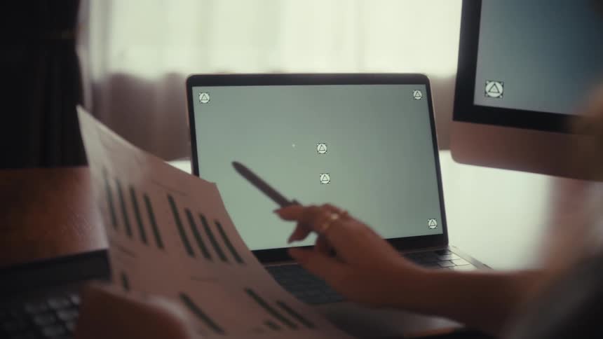 An over-the-shoulder shot of a businesswoman pointing at a green screen laptop while reviewing a printed business report
