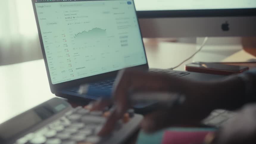 A financial professional analyzes stock market data on a laptop and uses a calculator for financial planning
