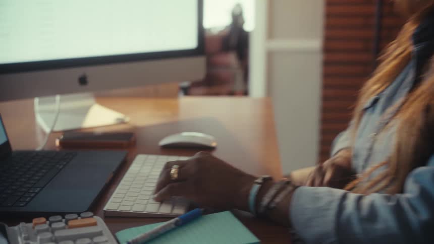 A professional African American woman works from her sunlit home office, analyzing data on her computer
