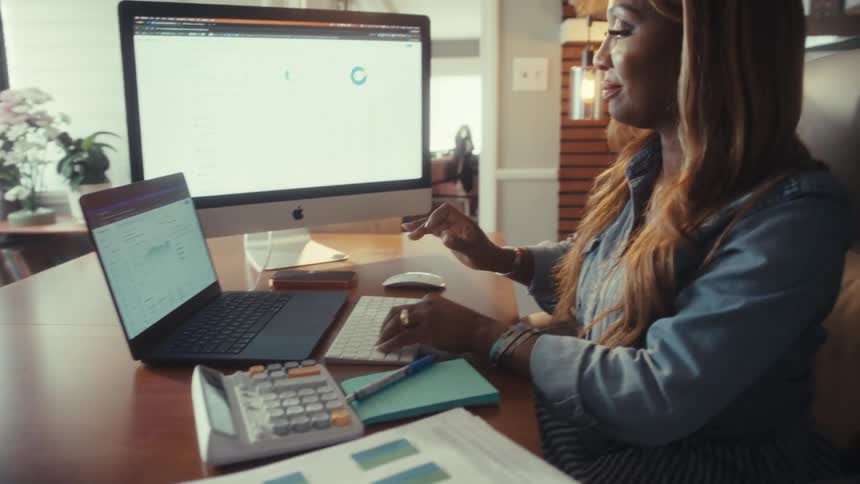 A focused woman works on her finances from her home office, typing on her keyboard before leaning back in her chair with a satisfied smile