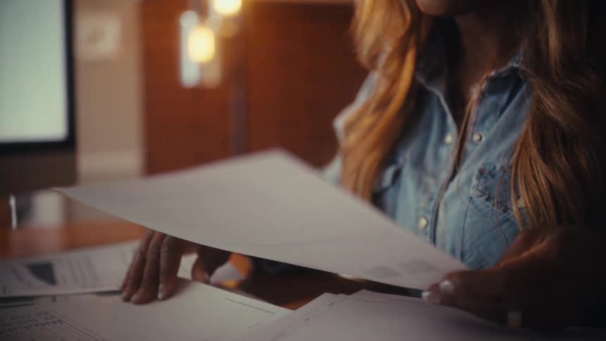 A close-up slow-motion shot of a businesswoman's hands sorting through financial reports and paperwork at her desk
