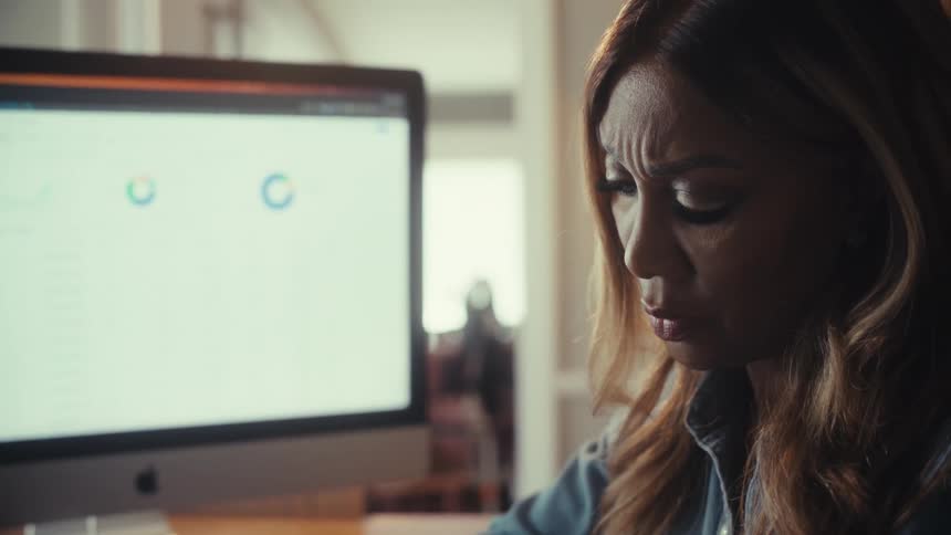 A focused businesswoman analyzes data on her computers, her face showing deep concentration and concern