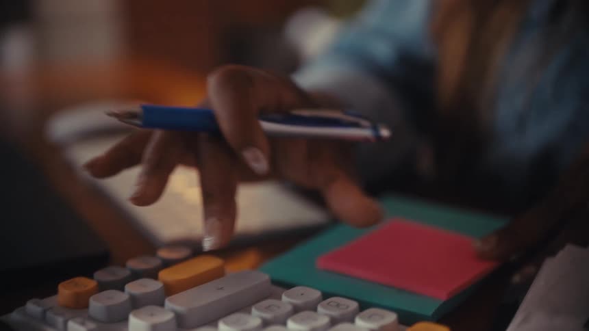 Close-up of a woman's hand using a calculator and holding a pen while working at a desk
