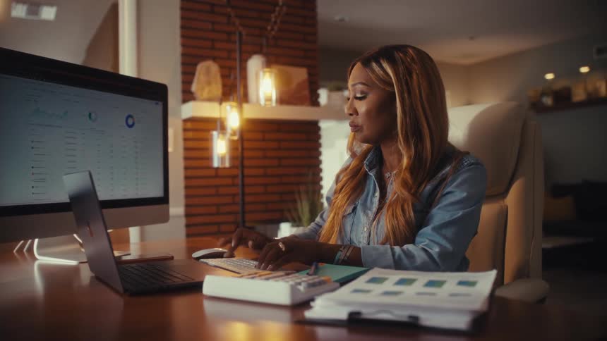 A professional woman analyzes business data and charts on her computer while working from her cozy home office