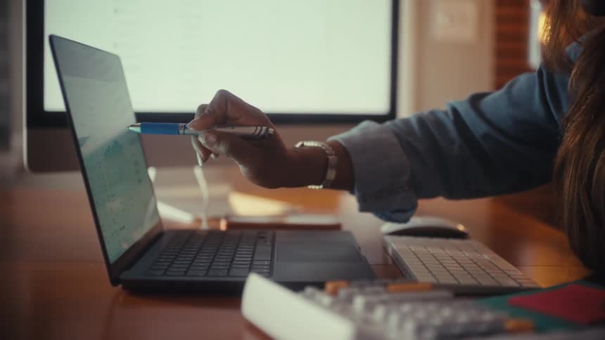 A woman meticulously manages her finances, using a calculator and referencing charts on her laptop at her home office desk