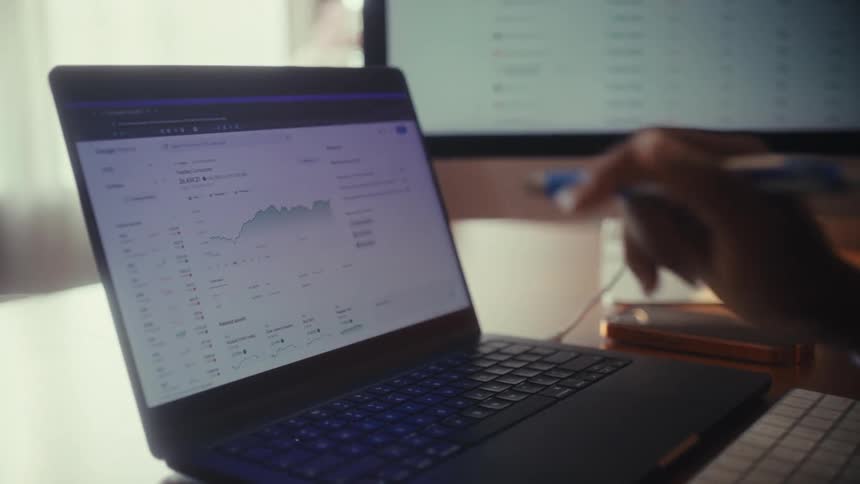 A businesswoman analyzes stock market trends on her laptop, using a calculator before pointing to a financial chart