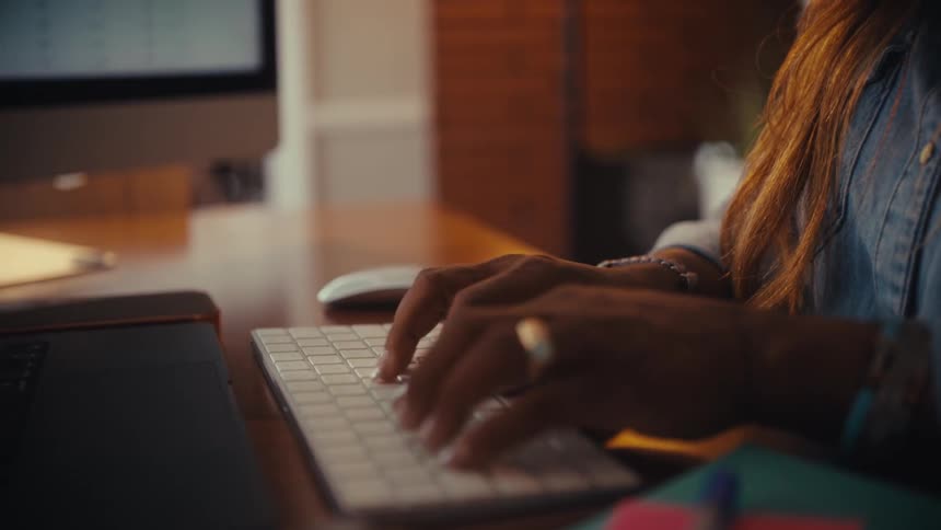 A close-up slow motion shot of a woman's hands typing on a wireless keyboard and using a mouse at her desk