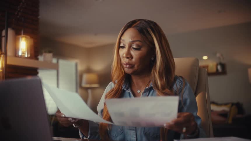 A professional woman reviews financial papers at her desk and smiles, happy with the successful outcome of her work