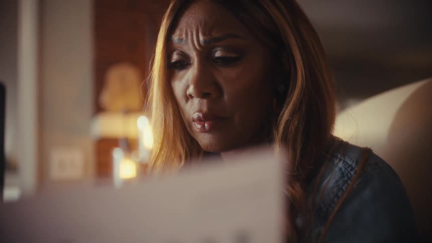A concerned woman with a furrowed brow carefully reviews financial charts and documents, feeling the weight of stress and worry