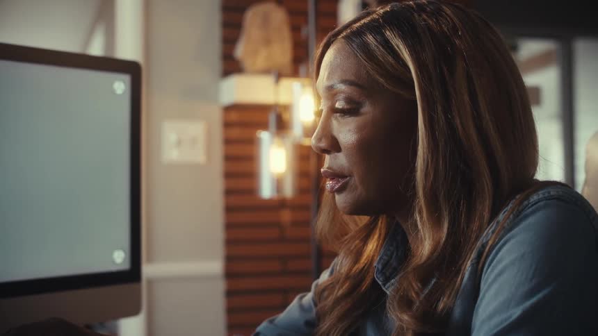Close up profile shot of a woman with long hair thoughtfully working on her computer in a home office