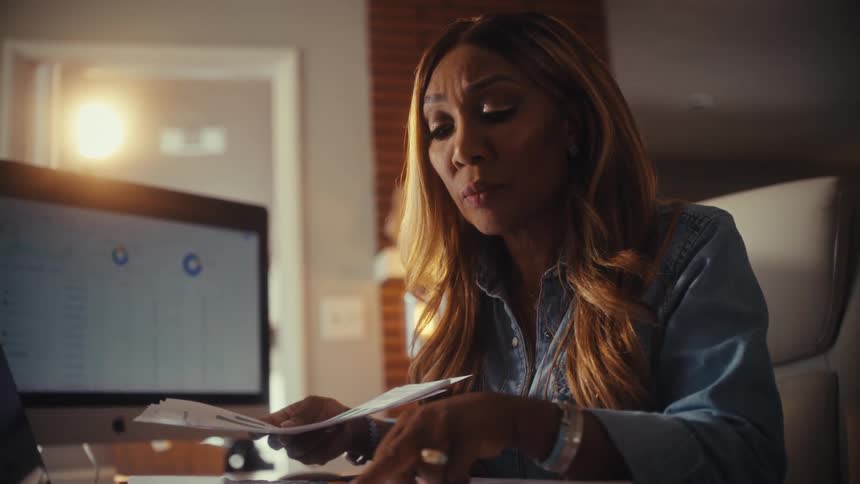 A focused woman meticulously analyzes financial charts and reports while working from her stylish home office in the evening