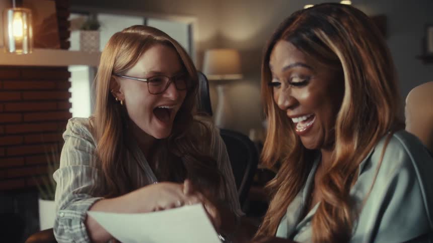 Two excited businesswomen shake hands and celebrate a successful agreement while looking at a document in an office