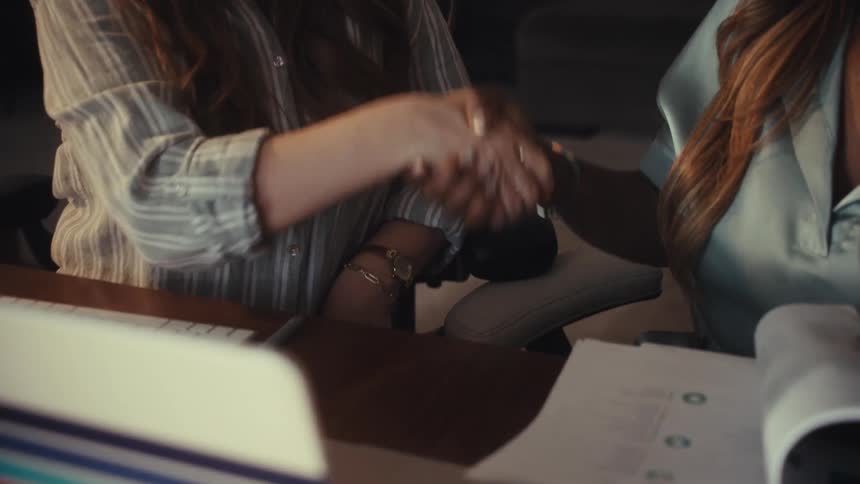 A close-up, slow-motion shot of two diverse businesswomen shaking hands over a desk to seal a deal