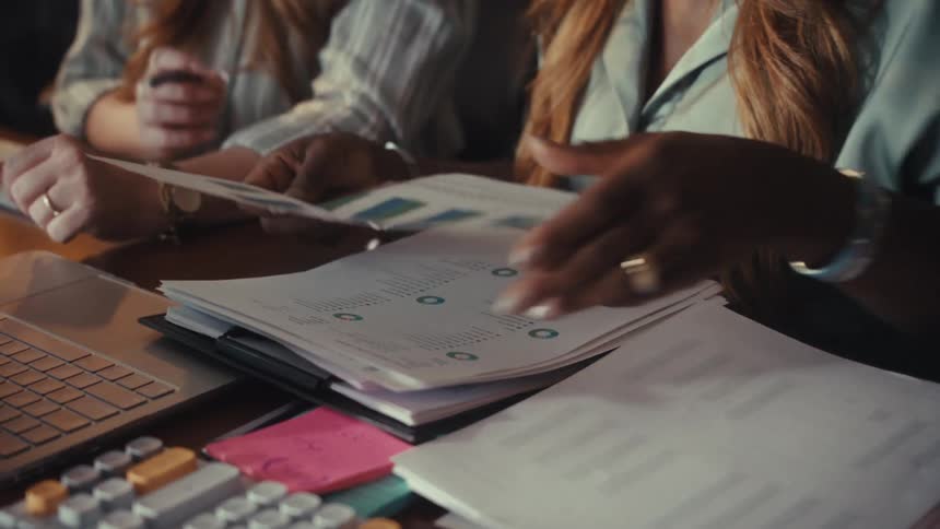 Close up slow motion shot of two women reviewing financial reports and charts together at an office desk