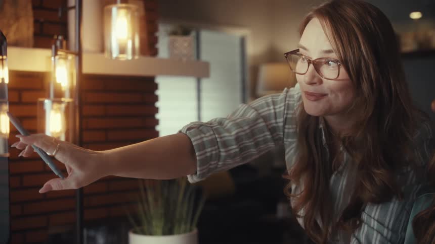 A creative professional woman with glasses explains her ideas while pointing at a screen with a stylus in a warmly lit office