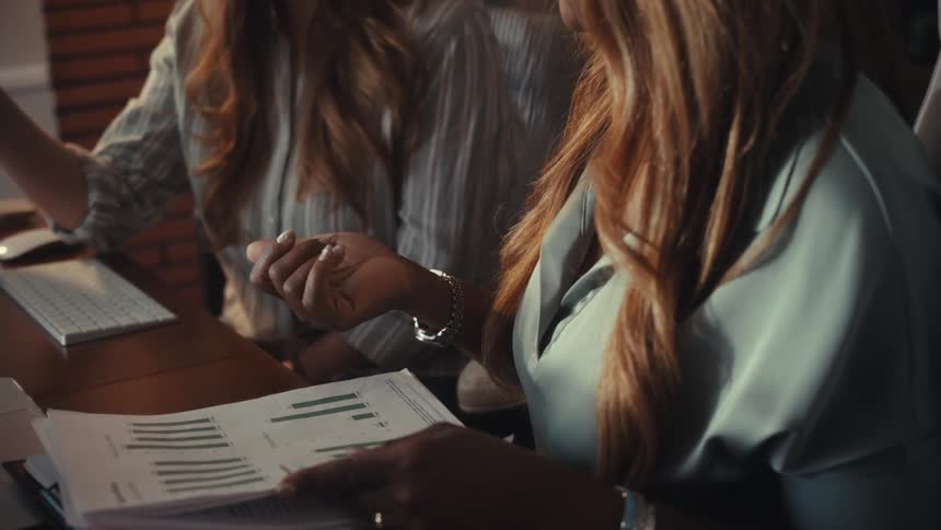 A close-up shot of two professional women collaborating and analyzing business data charts during an office meeting