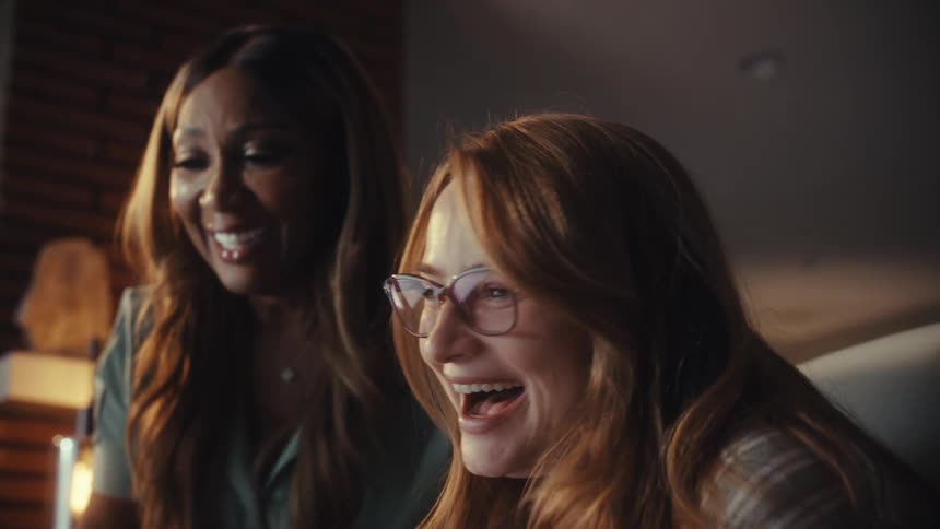 Excited diverse female colleagues celebrate success with a joyful hug while working late in a modern office