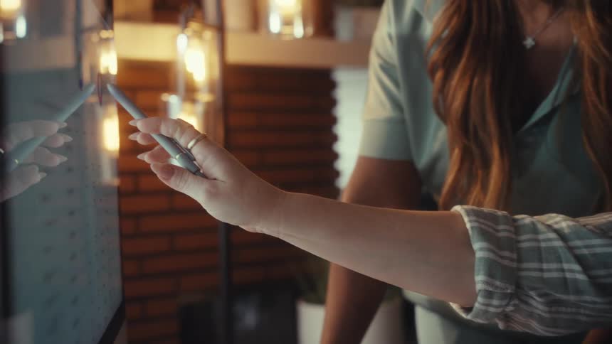 Close-up of a businesswoman's hand using a stylus to interact with data analytics on a large touchscreen monitor in a modern office