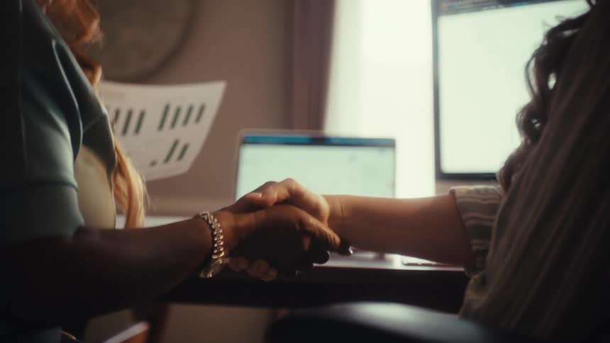 A close-up slow-motion shot of two businesswomen shaking hands to seal a deal in an office