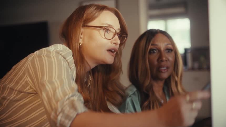 Two diverse professional women collaborate on a project, pointing and discussing details on a computer screen in a home office