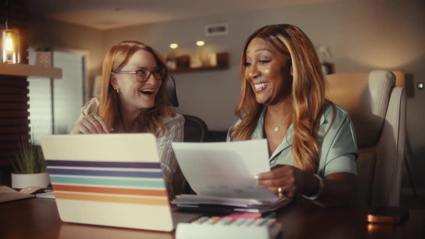 Two diverse female entrepreneurs celebrate a successful business deal with a happy handshake while working in their home office