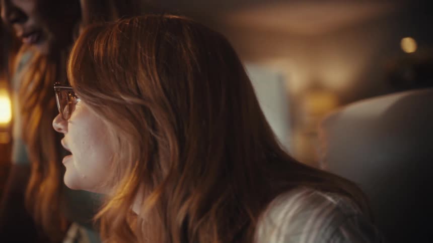 Profile shot of a focused woman with red hair and glasses collaborating with a female colleague in a warmly lit office