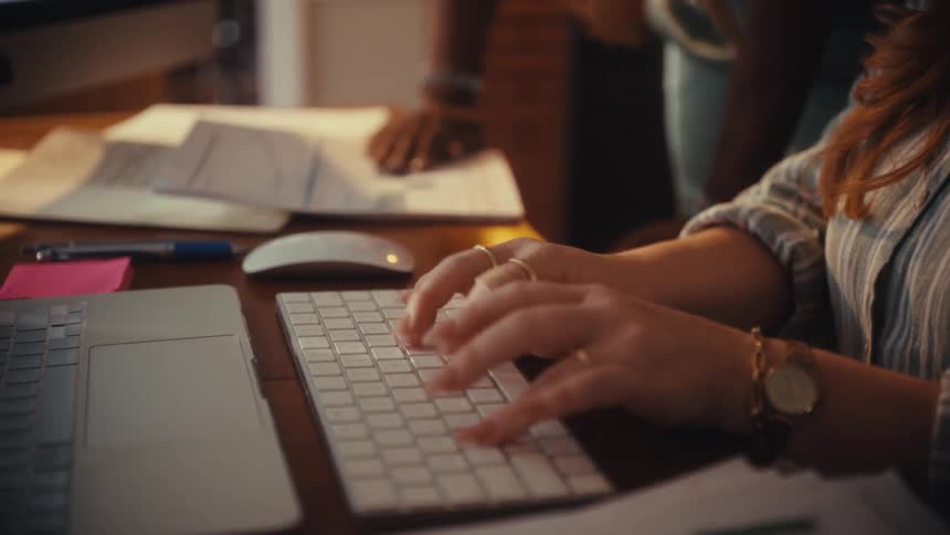 A close-up view of a woman's hands working and typing on a keyboard in a collaborative office environment
