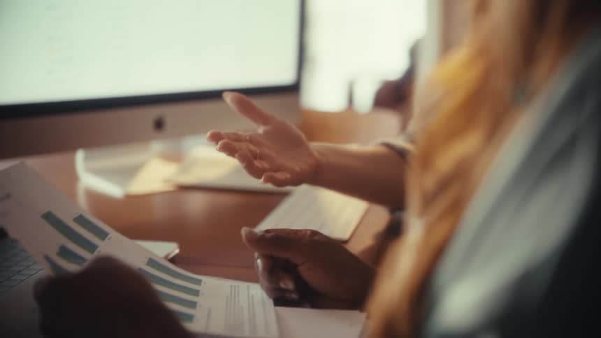 Over-the-shoulder slow motion shot of businesswomen analyzing financial charts and sealing a deal with a joyful handshake in the office