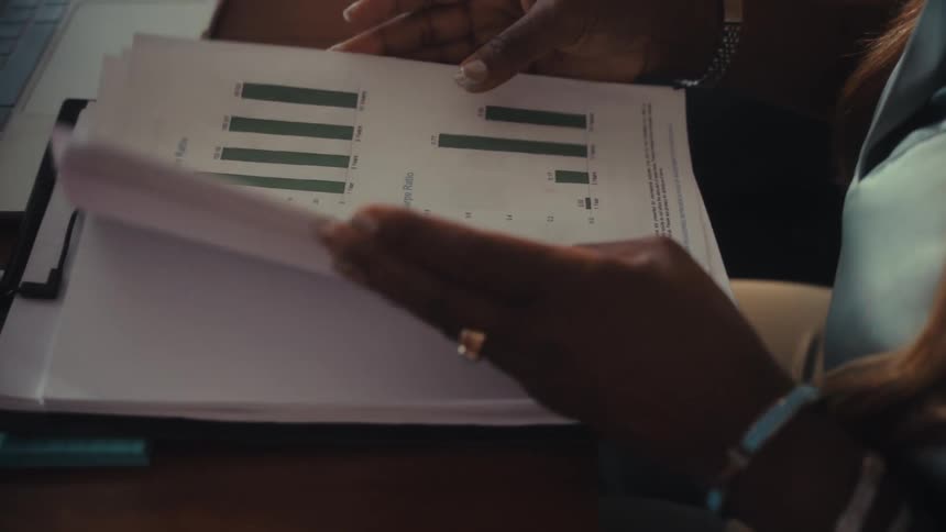 A businesswoman's hands flip through a stack of financial documents containing charts and graphs