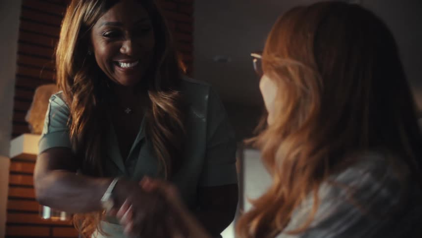 Two diverse professional women smile and shake hands in agreement after a successful meeting in a modern office